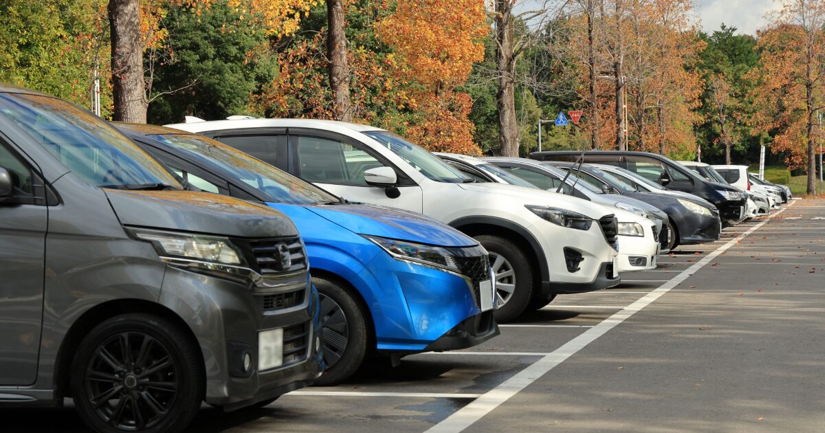 秋の木々に囲まれた駐車場と停車中の車