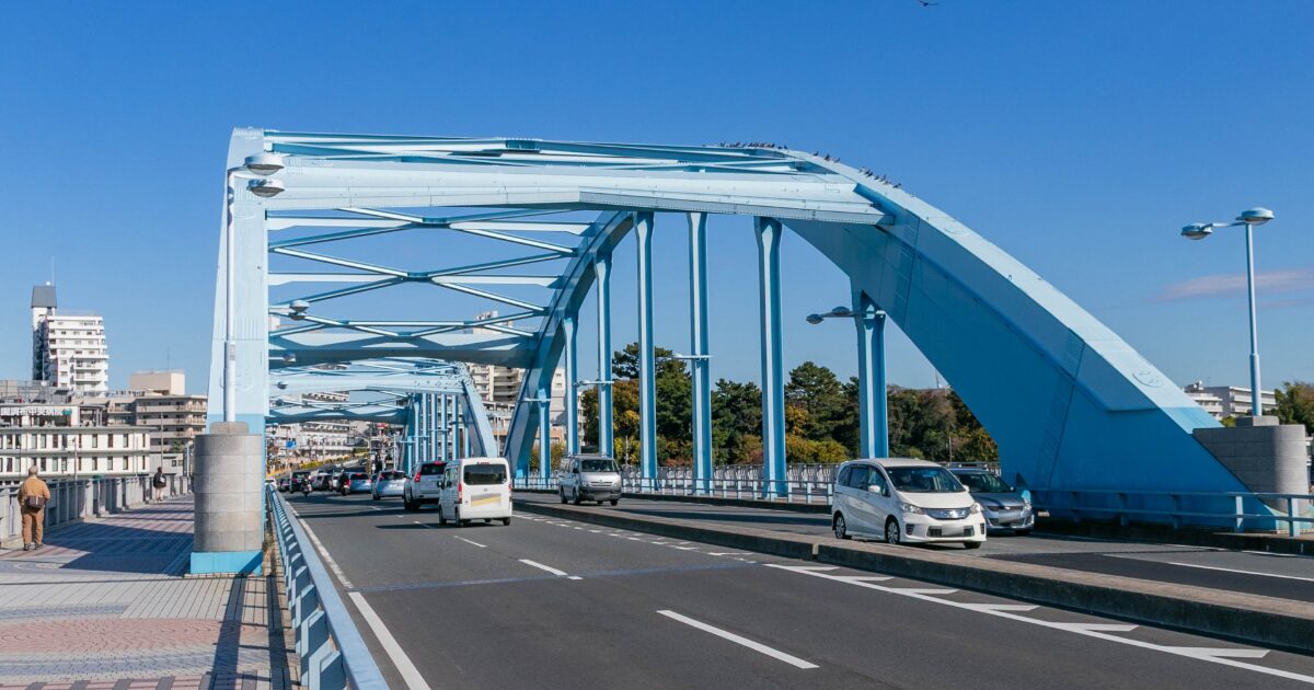 青い橋を走行する車と青空の街並み