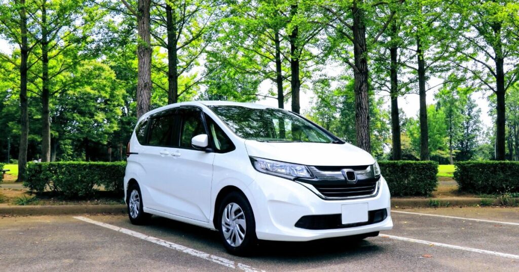 木立に囲まれた駐車場に停まる白いミニバン