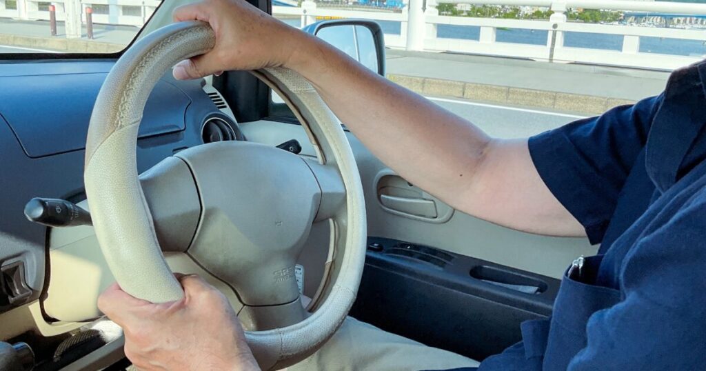 運転中の車内でハンドルを握る男性の手元