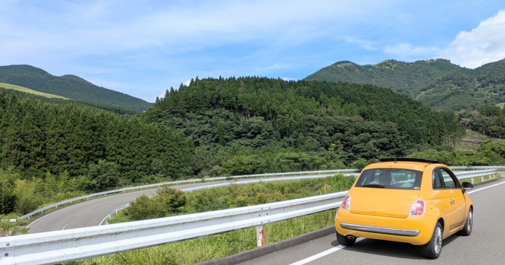 山間のカーブ道を走る黄色いコンパクトカー