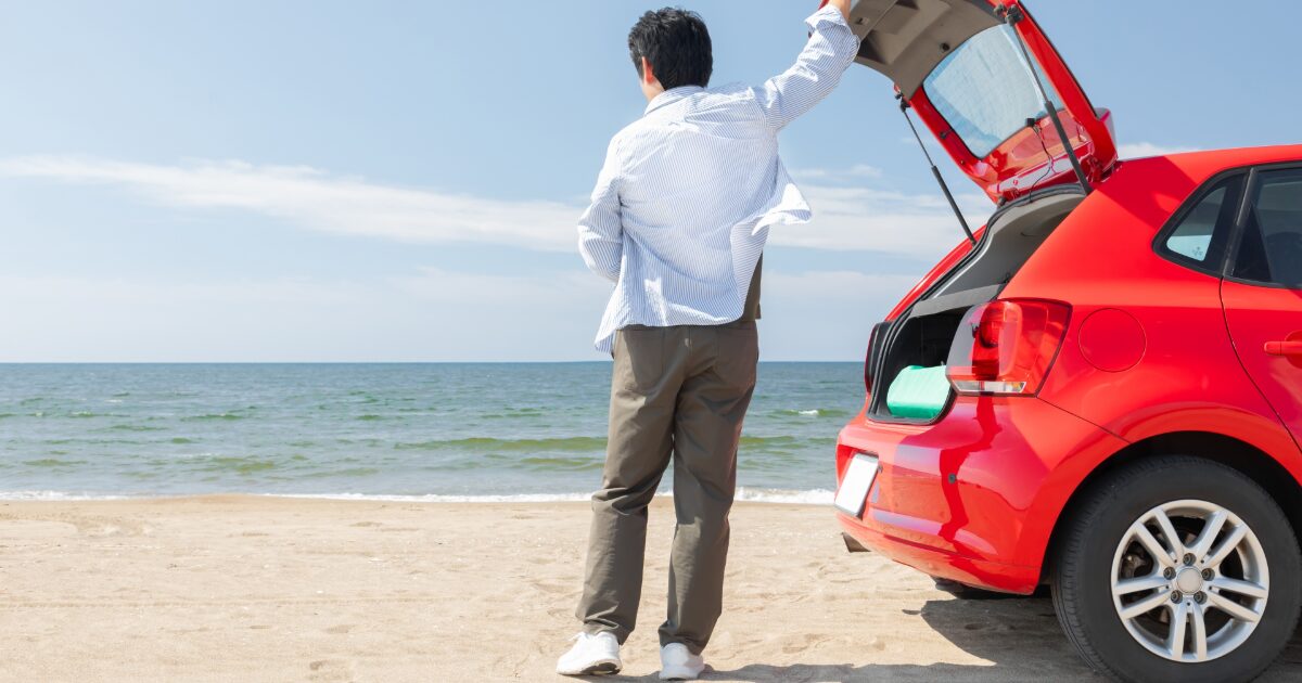 海辺に停車した赤い車と海を眺める男性